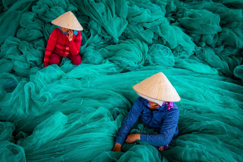 Ninh Binh - Ha Long 3D 2N Two women in traditional hats working with green fishing nets in Vietnam.